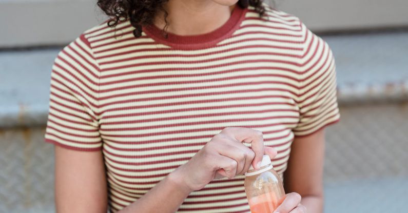 Digital Detoxing - Happy young ethnic female student with curly hair in trendy outfit smiling and looking away while drinking fresh juice sitting on stairs on street with modern laptop on knees