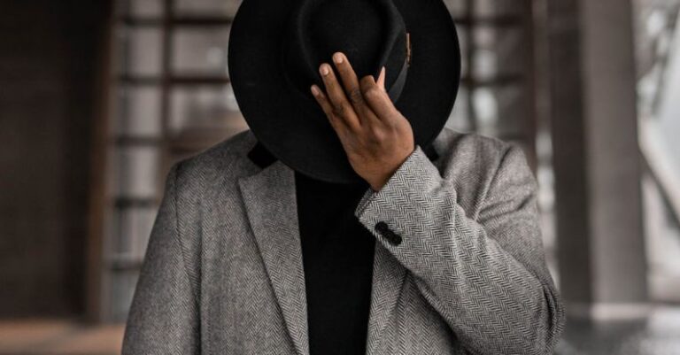 Gender-Neutral Fashion - Person in Gray Coat Holding Black Hat