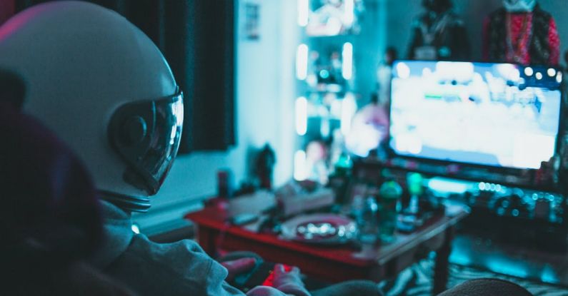 Reality TV Shows - Side view of unrecognizable person in virtual reality helmet sitting on sofa and playing with gamepad in dark room