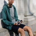 Virtual Fitness Coaches - Full body of young male in sportswear and VR goggles sitting on concrete foundation of white building and holding controllers