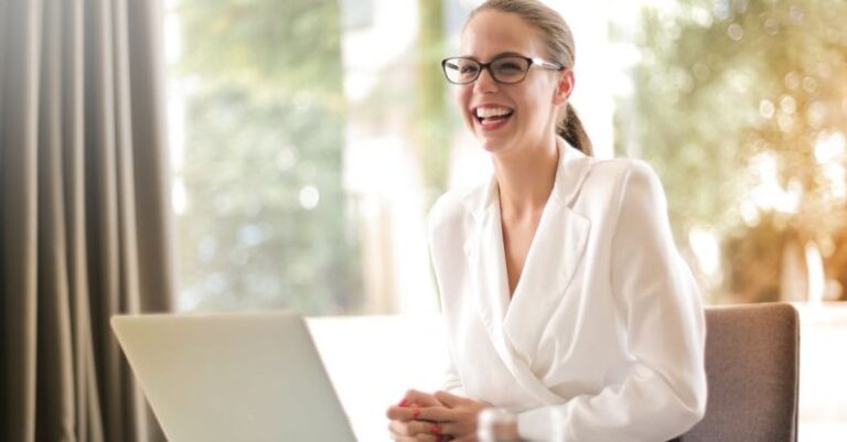 Employee Well-Being - Laughing businesswoman working in office with laptop